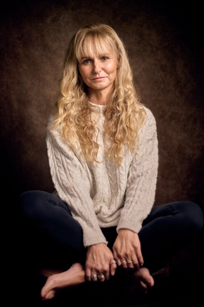 Portrait of woman with blonde hair and cream top sitting cross legged